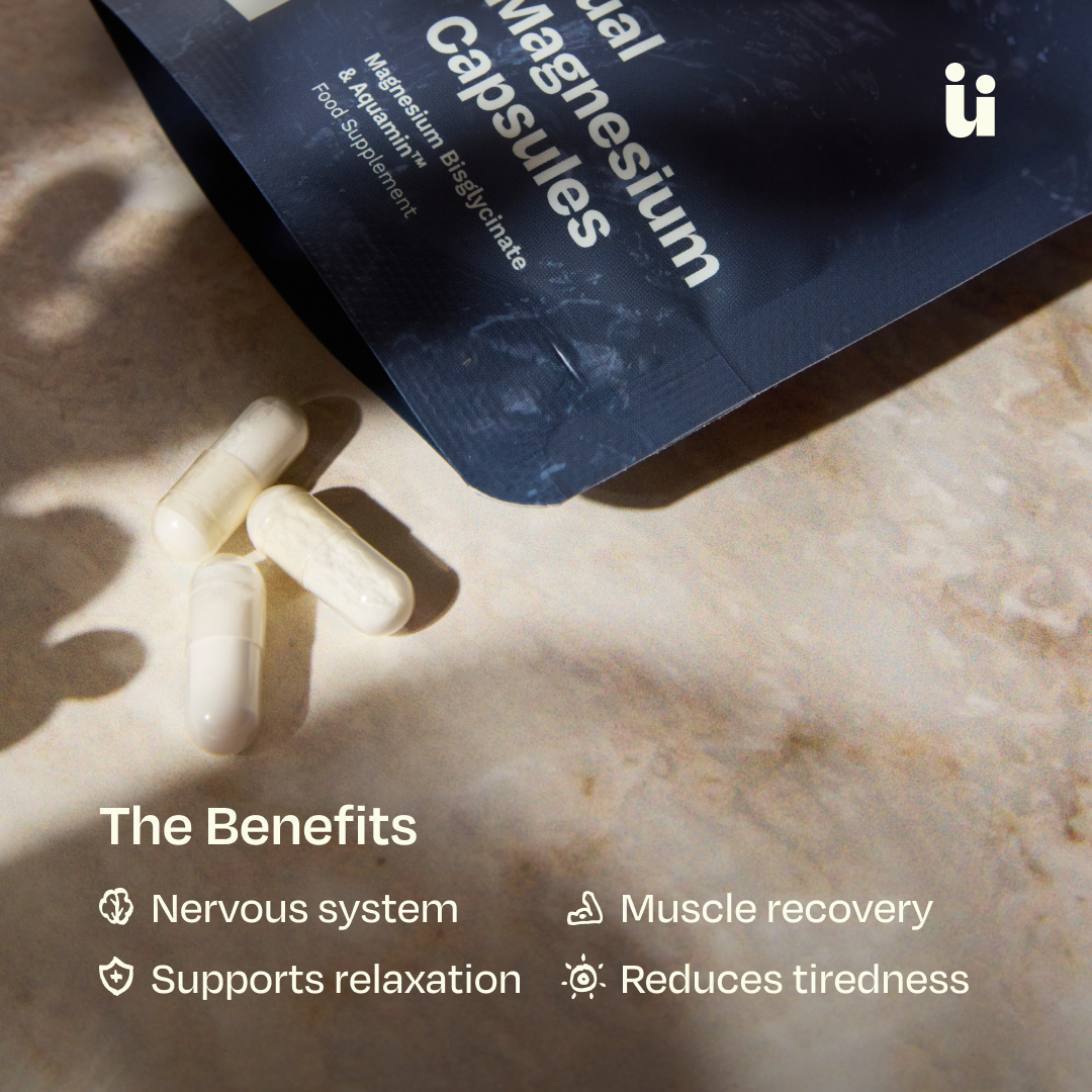 A dark blue pouch labeled 'Magnesium Capsules' lies open on a beige stone surface with three white capsules beside it. Text below reads 'The Benefits' with bullet points for nervous system, muscle recovery, supports relaxation, and reduces tiredness.